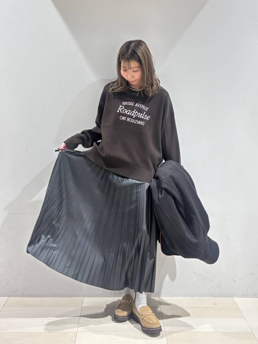 ブラック系のチェスターコート、ベージュ系のローファー、ブラック系のスカートを着用したレディースの秋コーディネートの9枚目の写真