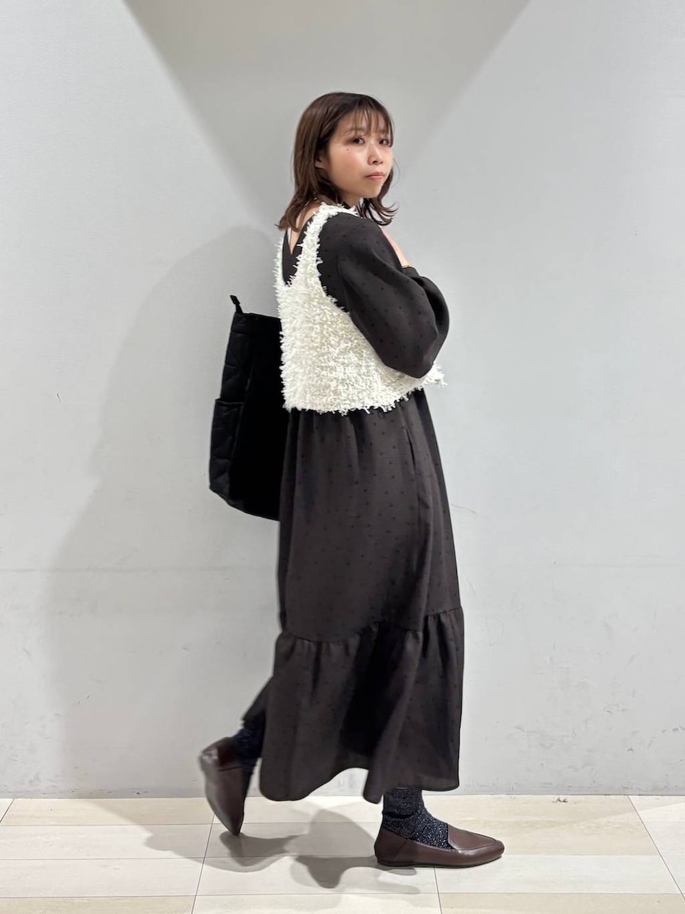 ブラック系のトートバッグ、ブラウン系のワンピース、ホワイト系のベストを着用したレディースの春コーディネートの5枚目の写真