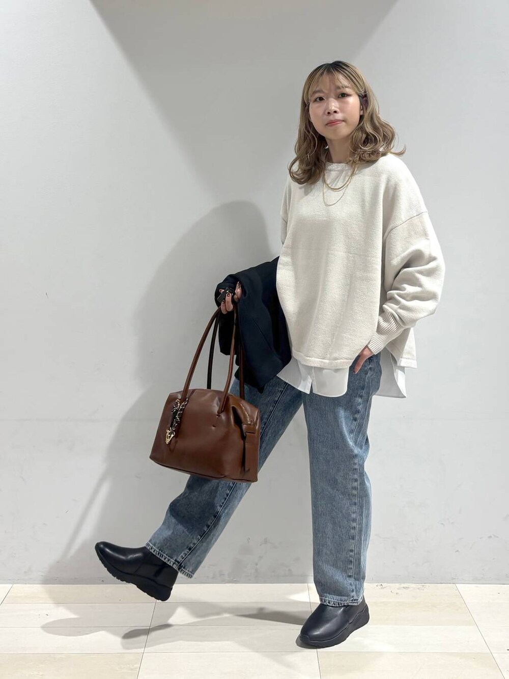 ベージュ系のニット/セーター、ブラウン系のボストンバッグ、ブルー系のデニムパンツを着用したレディースの秋コーディネートの2枚目の写真