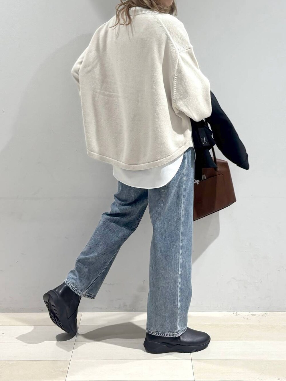 ベージュ系のニット/セーター、ブラウン系のボストンバッグ、ブルー系のデニムパンツを着用したレディースの秋コーディネートの5枚目の写真