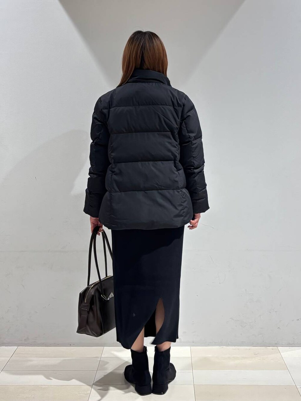 ブラウン系のボストンバッグ、ブラック系のダウンジャケット/コート、ブラック系のスカートを着用したレディースの冬コーディネートの5枚目の写真