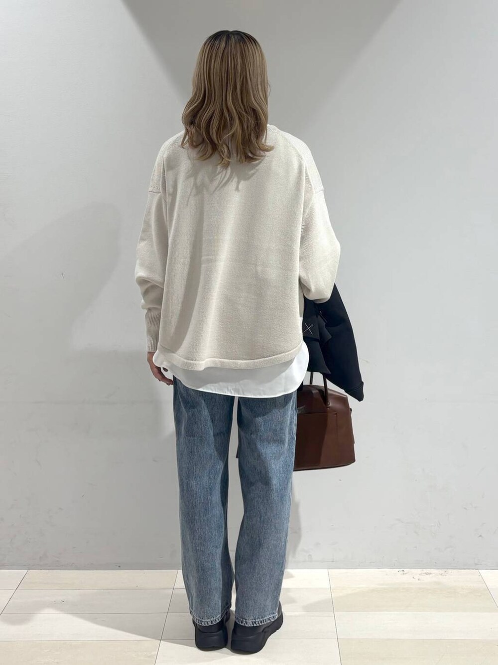 ベージュ系のニット/セーター、ブラウン系のボストンバッグ、ブルー系のデニムパンツを着用したレディースの秋コーディネートの4枚目の写真