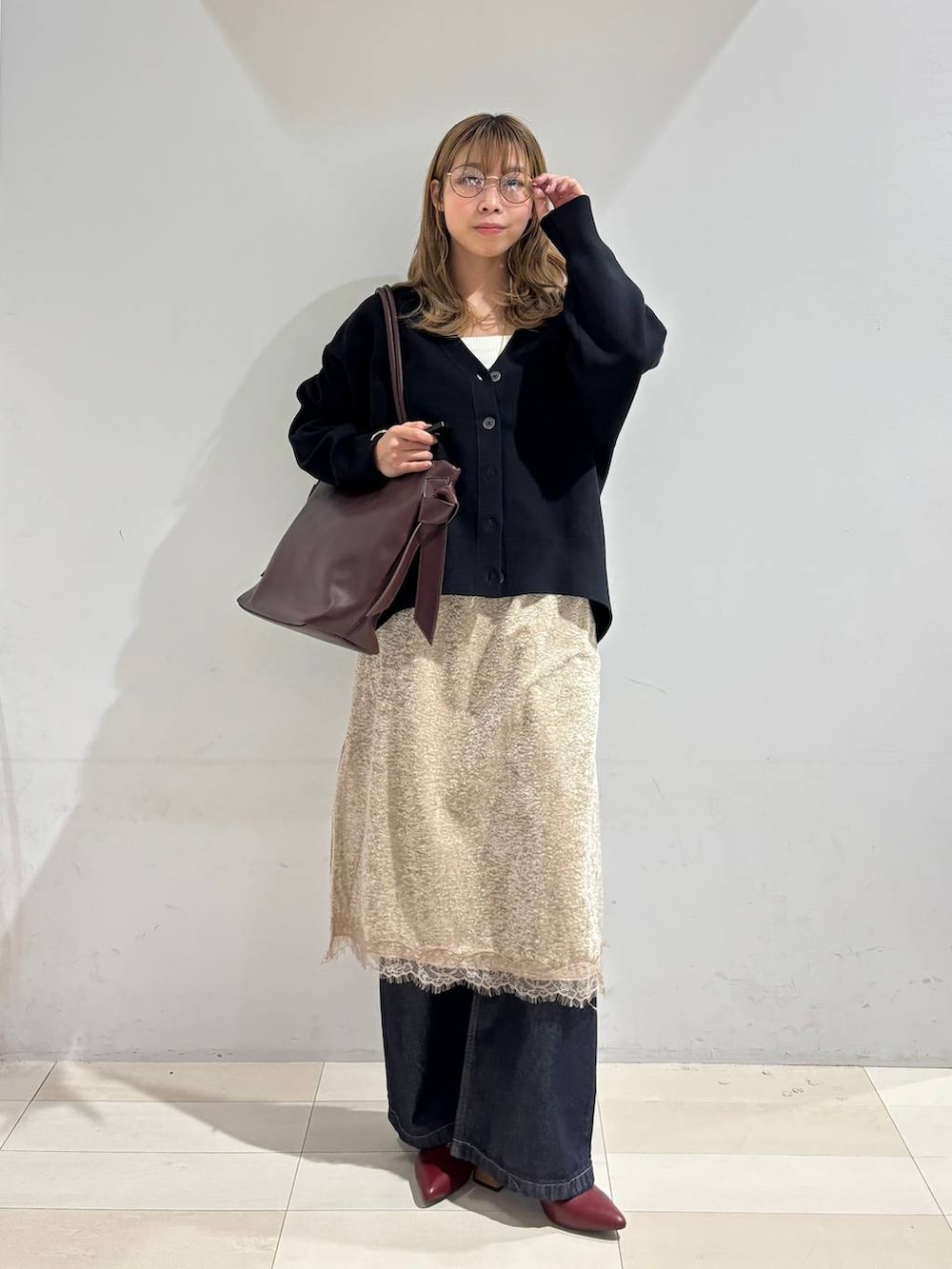 レッド系のトートバッグ、ブラック系のカーディガン/ボレロ、ブルー系のデニムパンツを着用したレディースの秋コーディネートの8枚目の写真