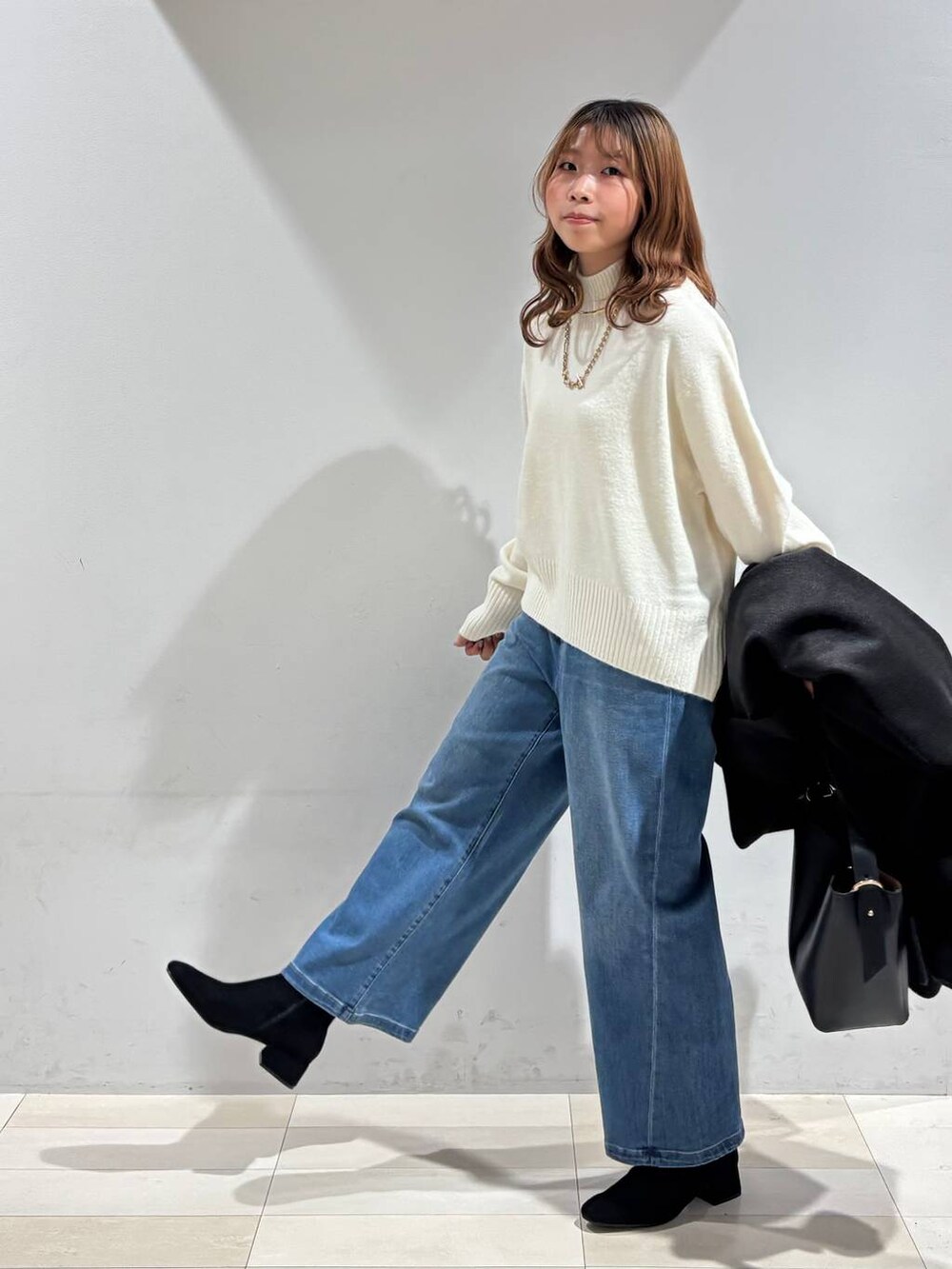 ブラック系のショルダーバッグ、ブラック系のチェスターコート、ホワイト系のニット/セーターを着用したレディースの冬コーディネートの2枚目の写真