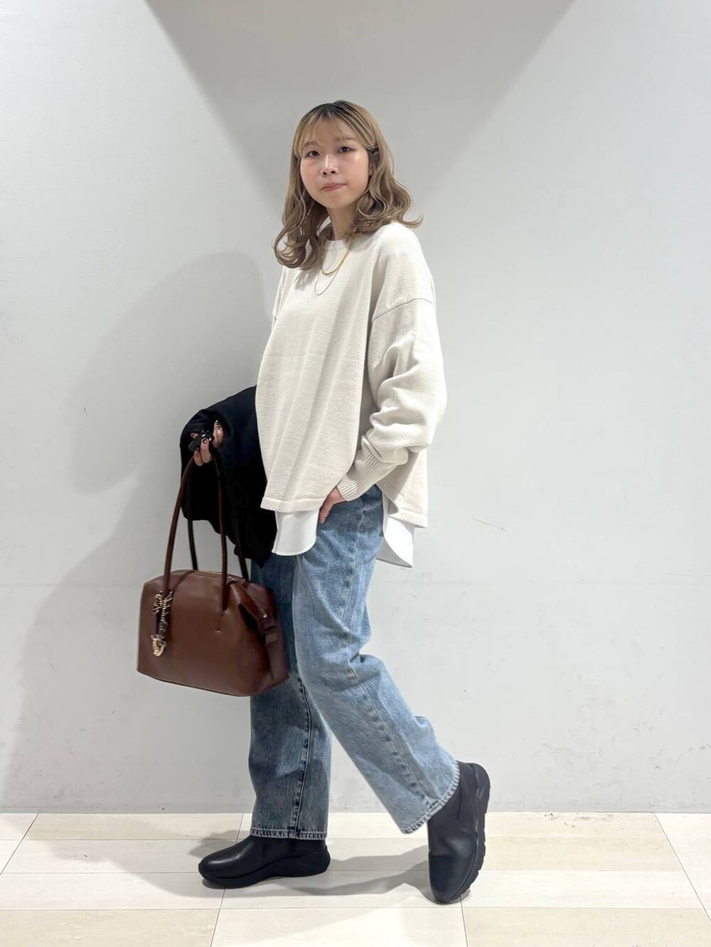 ベージュ系のニット/セーター、ブラウン系のボストンバッグ、ブルー系のデニムパンツを着用したレディースの秋コーディネートの3枚目の写真