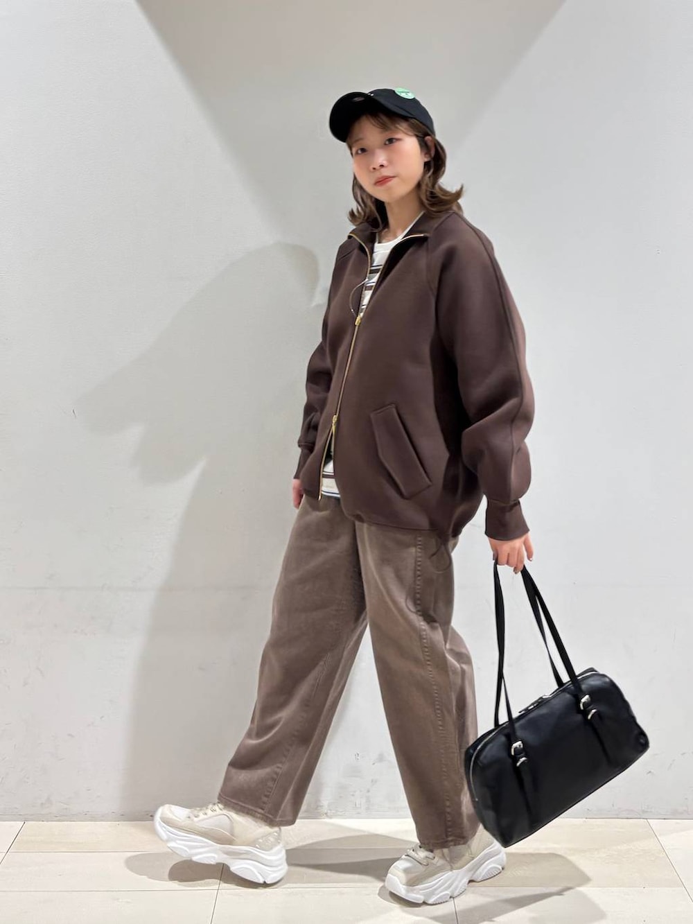 ブラウン系のデニムパンツ、ブラウン系のブルゾン、ゴールド系のスニーカーを着用したレディースの春コーディネートの4枚目の写真