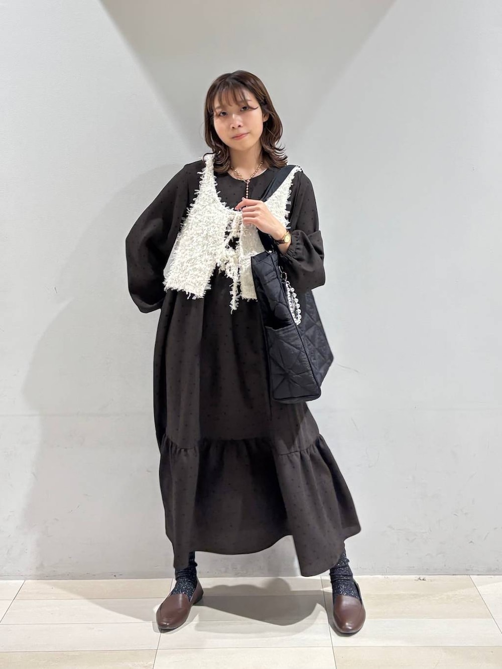 ブラック系のトートバッグ、ブラウン系のワンピース、ホワイト系のベストを着用したレディースの春コーディネートの7枚目の写真