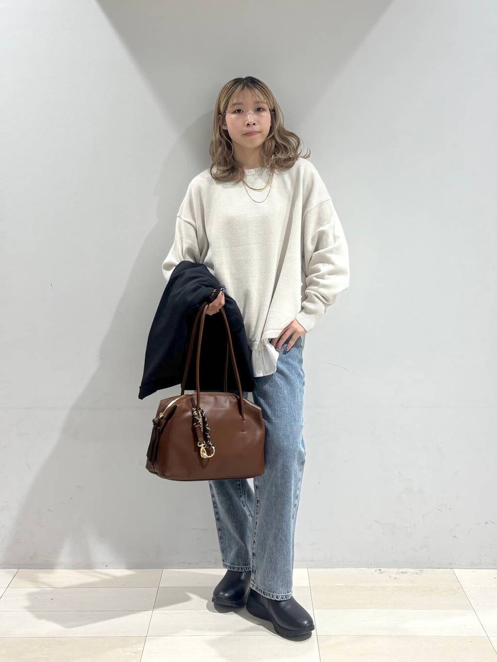ベージュ系のニット/セーター、ブラウン系のボストンバッグ、ブルー系のデニムパンツを着用したレディースの秋コーディネートの8枚目の写真
