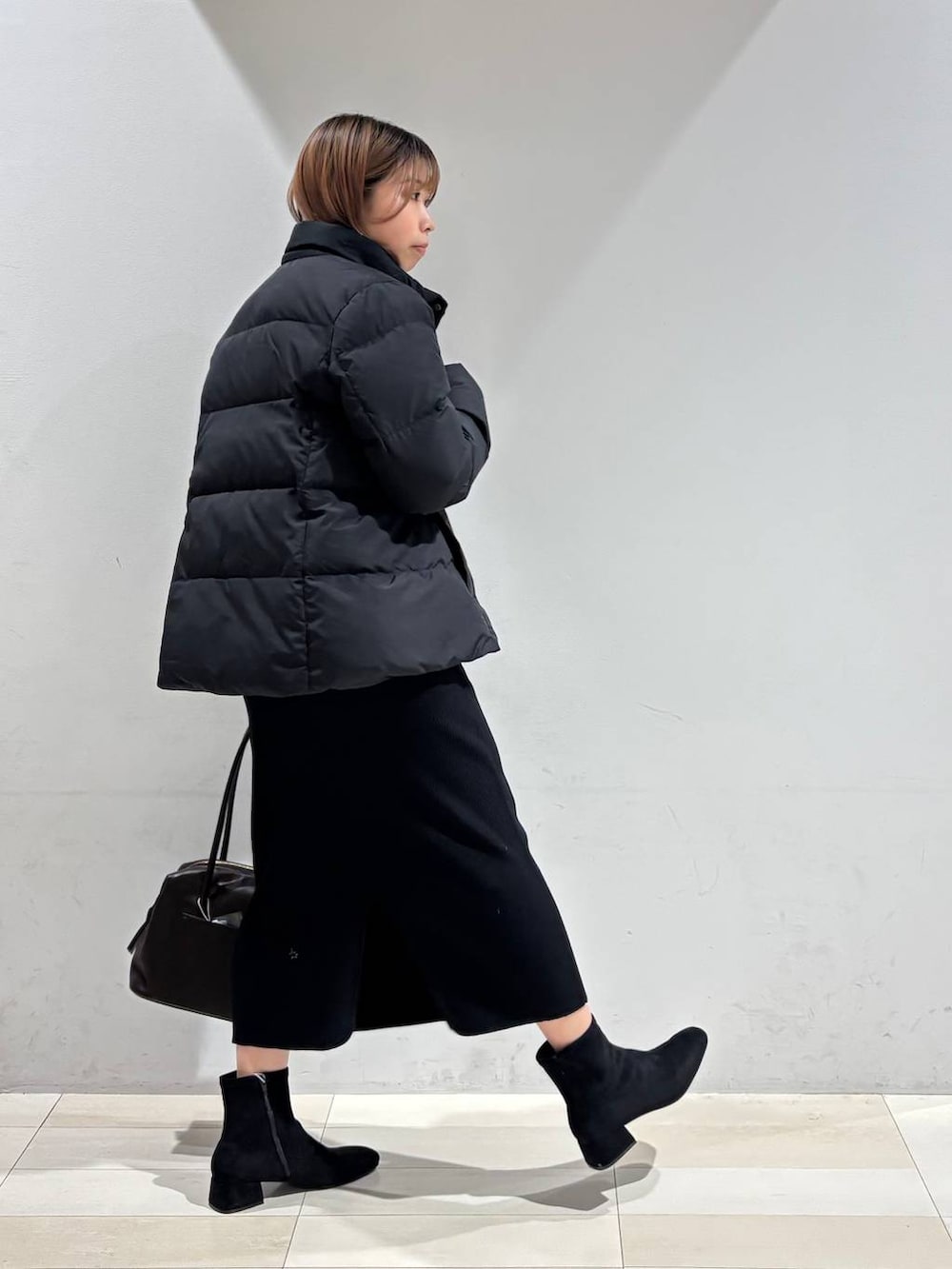 ブラウン系のボストンバッグ、ブラック系のダウンジャケット/コート、ブラック系のスカートを着用したレディースの冬コーディネートの6枚目の写真