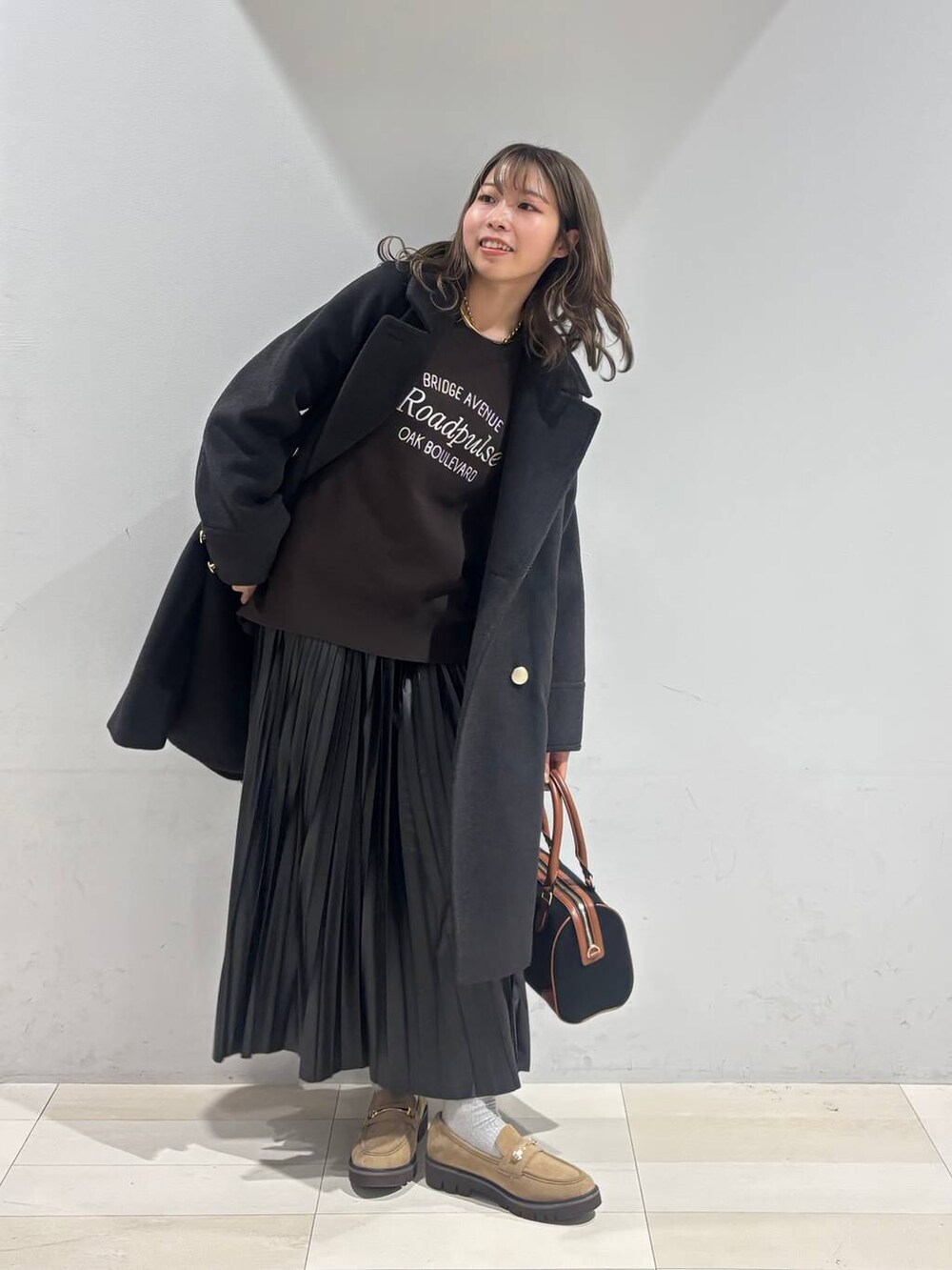 ブラック系のチェスターコート、ベージュ系のローファー、ブラック系のスカートを着用したレディースの秋コーディネートの4枚目の写真