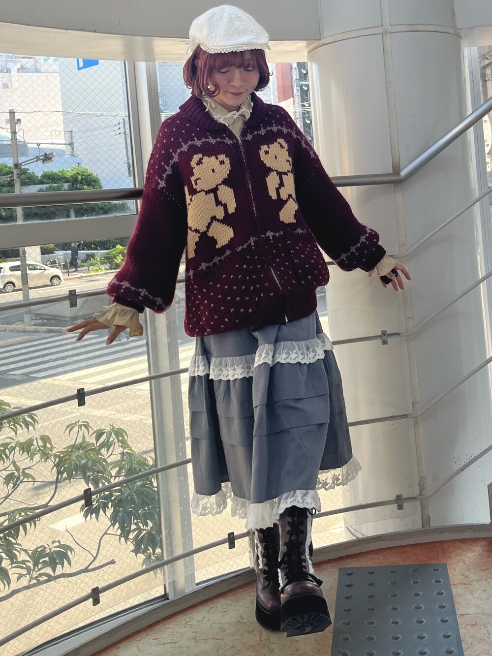 レッド系のカーディガン/ボレロ、グレー系のスカート、ブラック系のブーツを着用したレディースの秋コーディネートの2枚目の写真