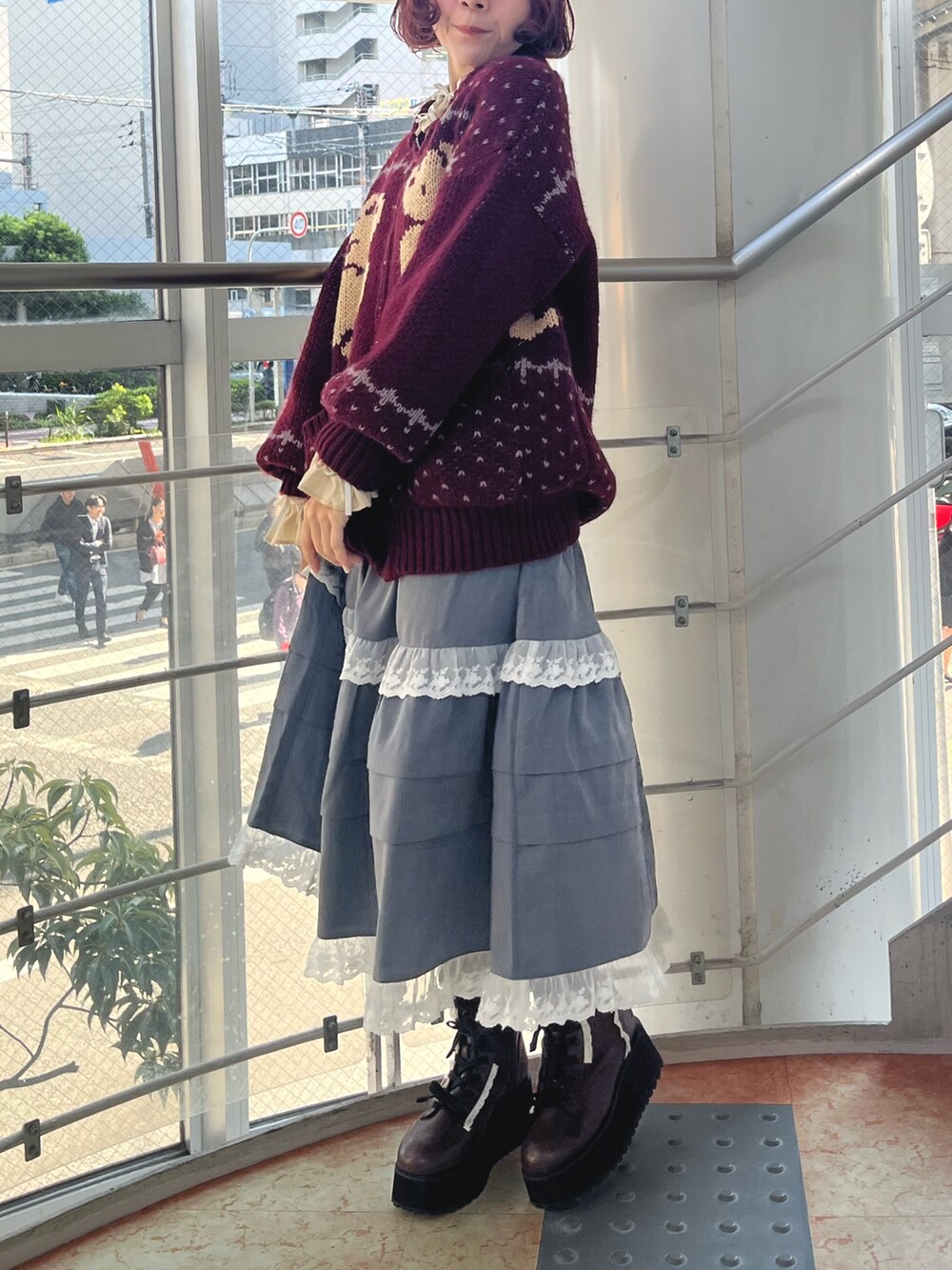 レッド系のカーディガン/ボレロ、グレー系のスカート、ブラック系のブーツを着用したレディースの秋コーディネートの3枚目の写真