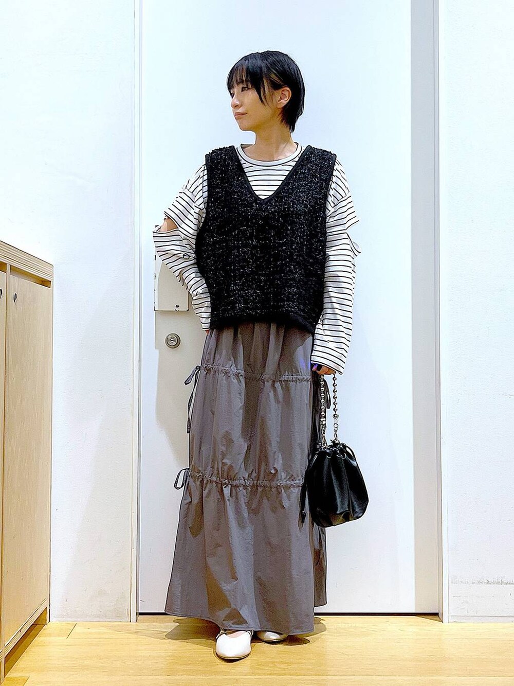 ブラック系のショルダーバッグ、ホワイト系のパンプス、グレー系のスカートを着用したレディースの秋コーディネートの2枚目の写真