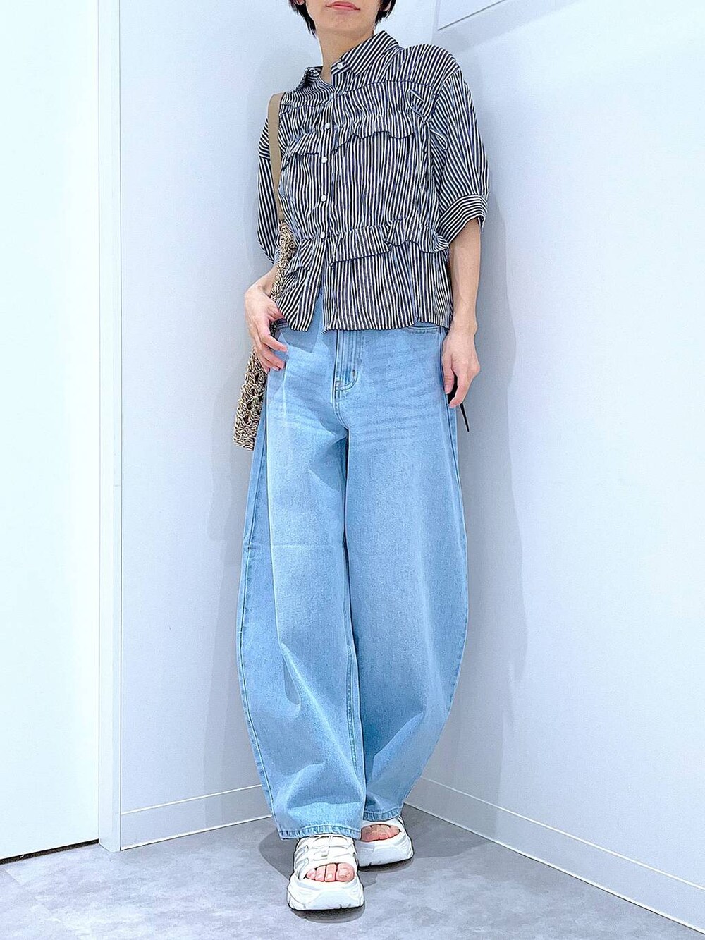 ブルー系のデニムパンツ、ベージュ系のトートバッグ、ホワイト系のスニーカーを着用したレディースの夏コーディネートの3枚目の写真