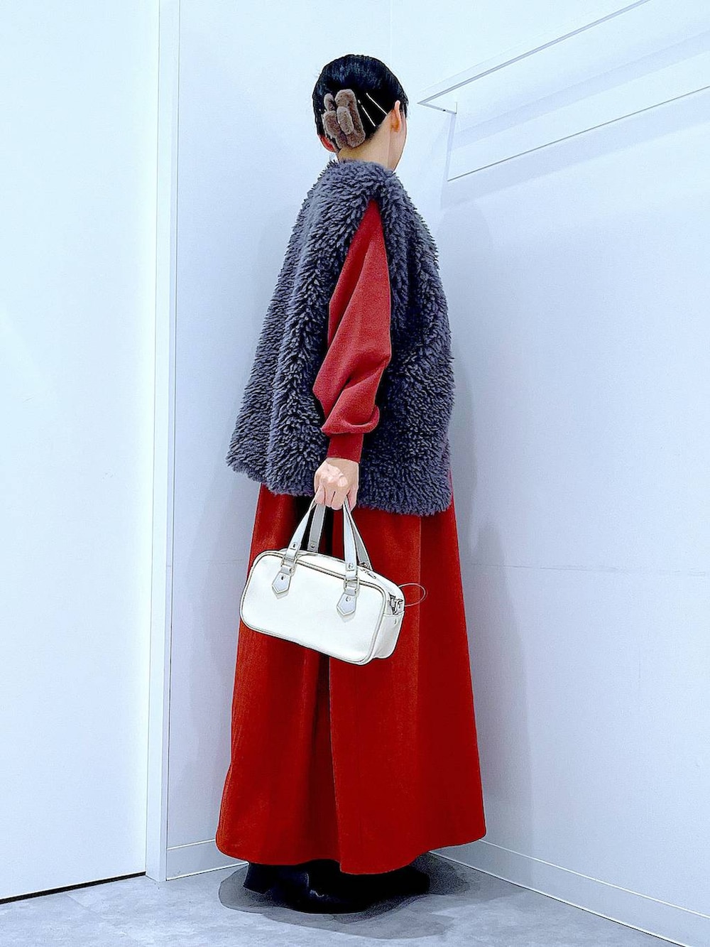 グレー系のベスト、ブラック系のブーツ、ホワイト系のショルダーバッグを着用したレディースの秋コーディネートの4枚目の写真