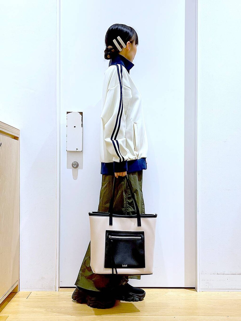 ホワイト系のトートバッグ、ブラック系のブーツ、グリーン系のスカートを着用したレディースの冬コーディネートの4枚目の写真