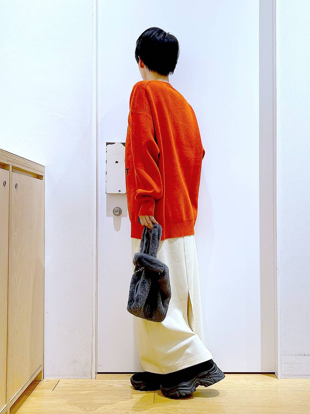 グレー系のショルダーバッグ、オレンジ系のニット/セーター、ブラック系のブーツを着用したレディースの冬コーディネートの3枚目の写真