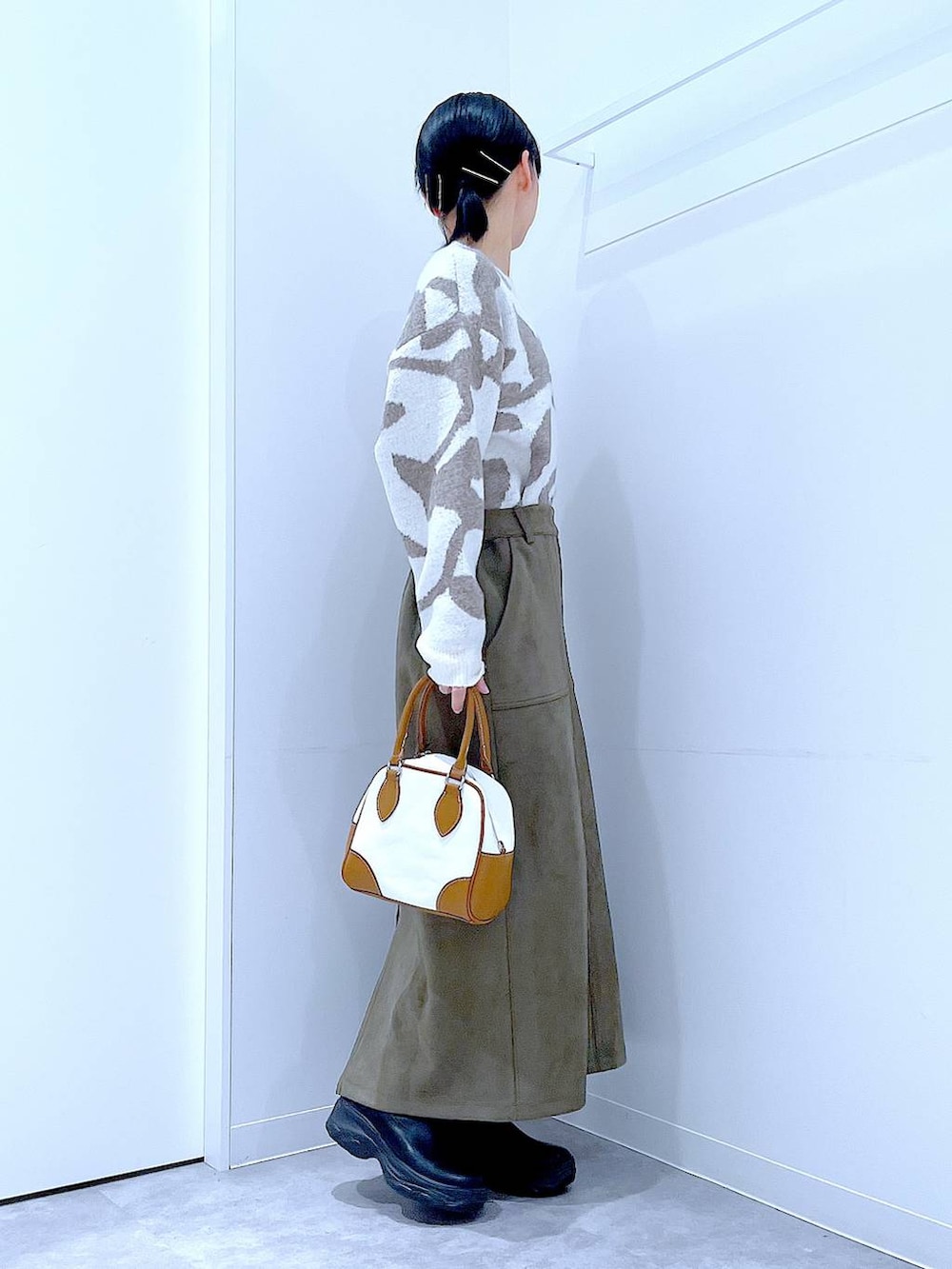 ブラック系のブーツ、ホワイト系のハンドバッグ、グリーン系のスカートを着用したレディースの秋コーディネートの4枚目の写真