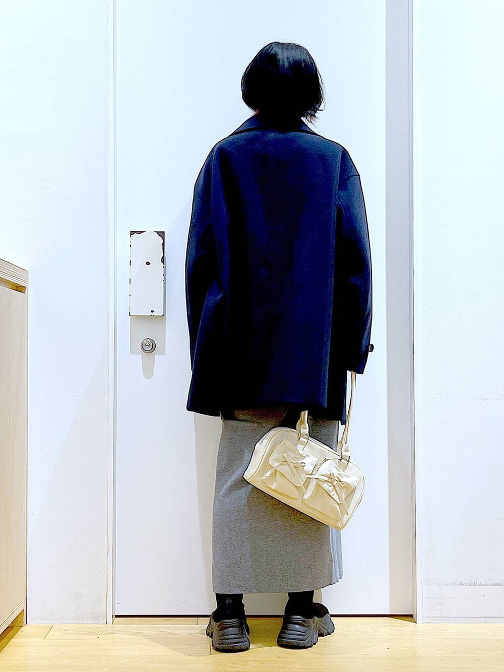 ブルー系のステンカラーコート、ホワイト系のハンドバッグ、ブラック系のブーツを着用したレディースの冬コーディネートの5枚目の写真