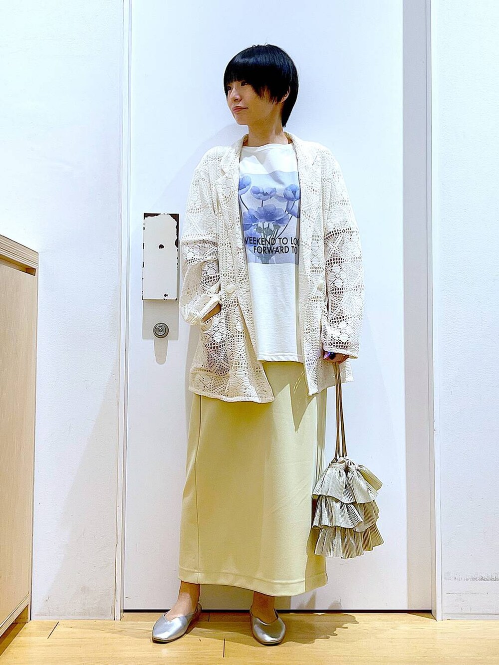 シルバー系のパンプス、ベージュ系のショルダーバッグ、イエロー系のスカートを着用したレディースの春コーディネートの2枚目の写真