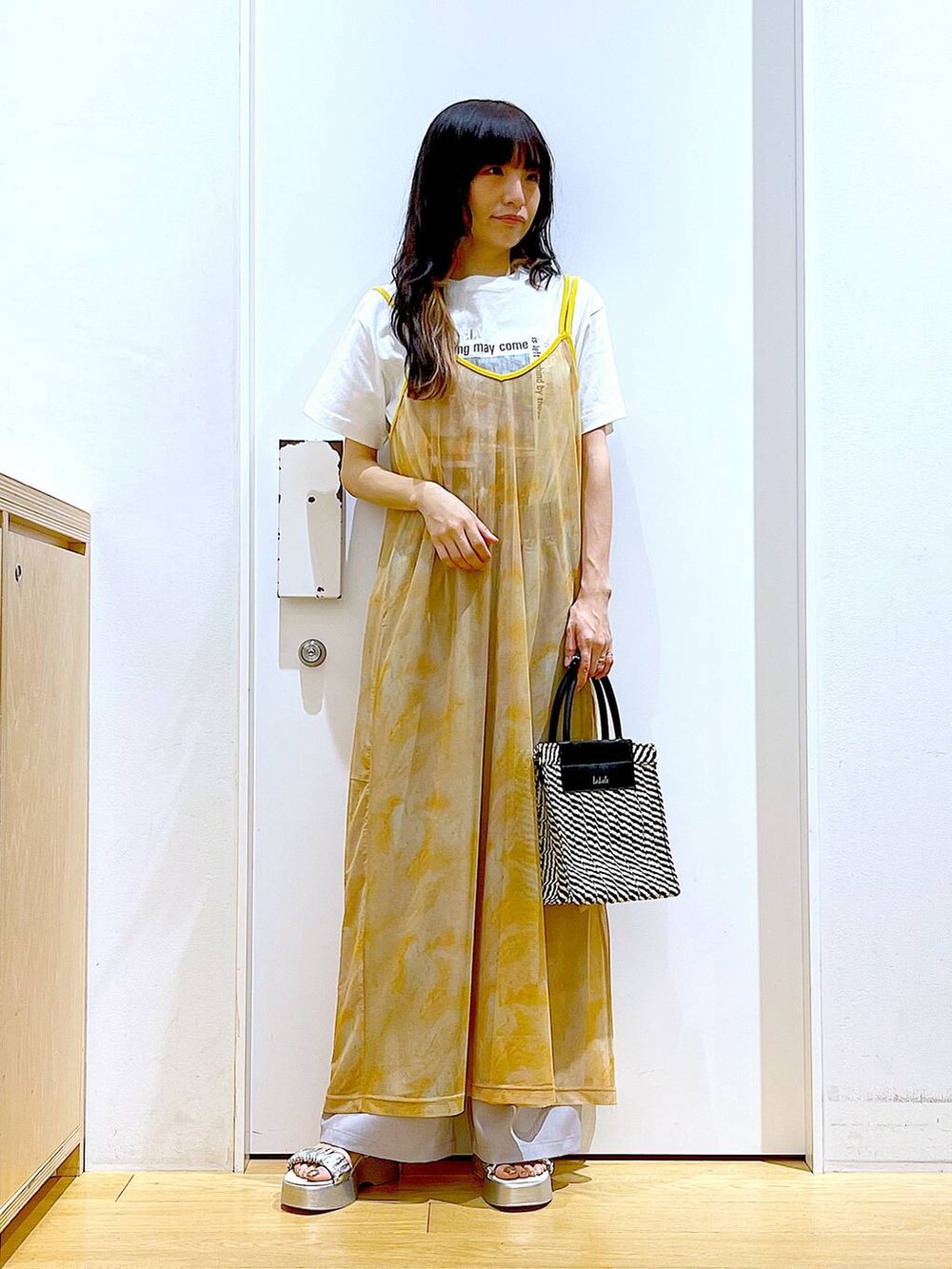 シルバー系のサンダル、オレンジ系のワンピース、ブラック系のショルダーバッグを着用したレディースの夏コーディネートの2枚目の写真