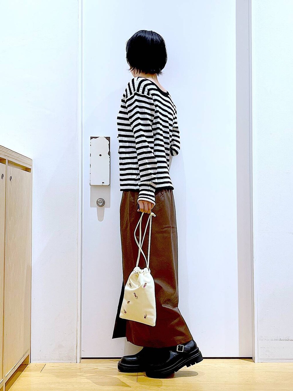 ブラウン系のスカート、ホワイト系のショルダーバッグ、ブラック系のブーツを着用したレディースの秋コーディネートの3枚目の写真