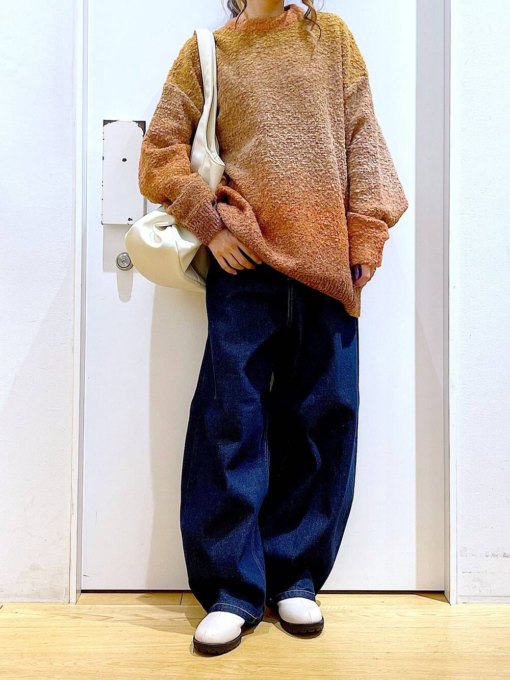 オレンジ系のニット/セーター、ホワイト系のトートバッグ、ベージュ系のブーツを着用したレディースの冬コーディネートの6枚目の写真