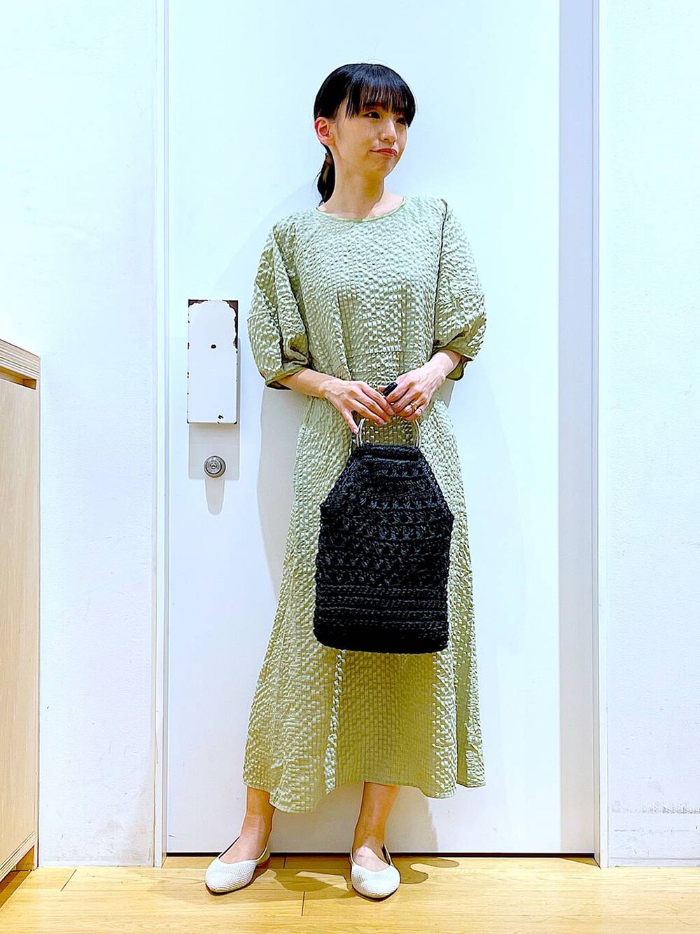 グリーン系のワンピース、ホワイト系のパンプス、ブラック系のハンドバッグを着用したレディースの春コーディネートの2枚目の写真