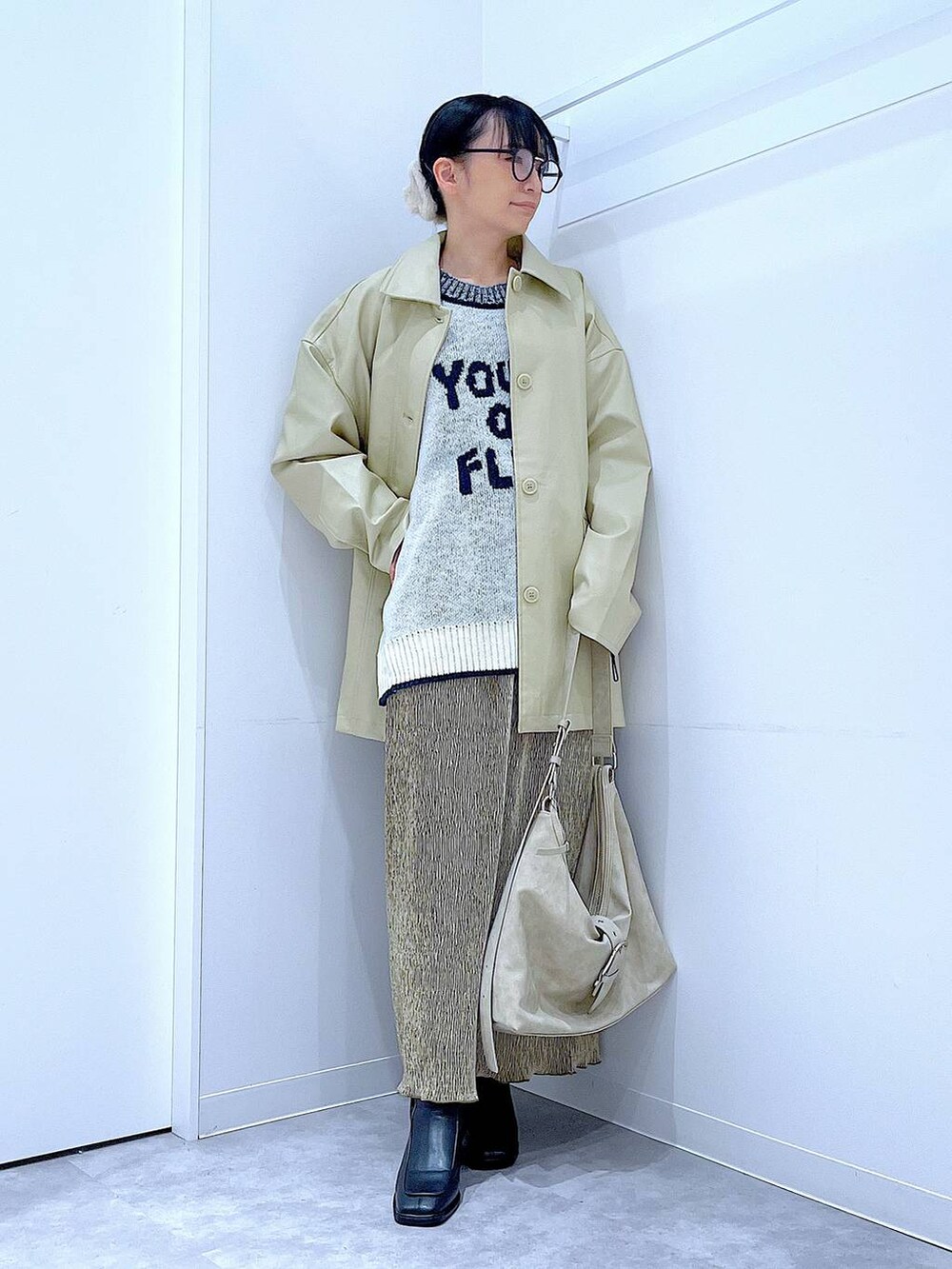 ベージュ系のステンカラーコート、ブラック系のブーツ、ホワイト系のショルダーバッグを着用したレディースの冬コーディネートの2枚目の写真