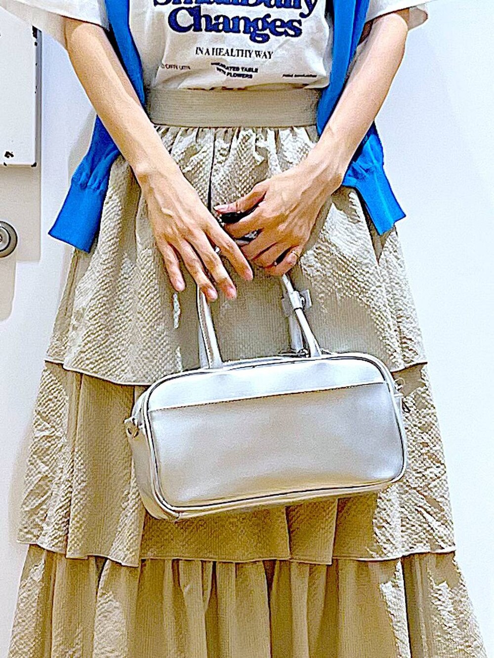 シルバー系のショルダーバッグ、ブルー系のカーディガン/ボレロ、ホワイト系のパンプスを着用したレディースの春コーディネートの9枚目の写真