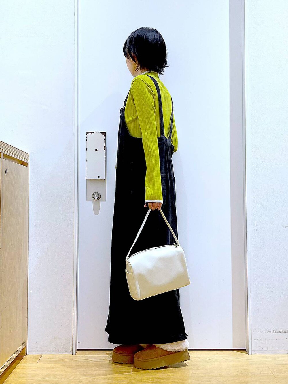 グレー系のジャンパースカート、ホワイト系のショルダーバッグ、グリーン系のニット/セーターを着用したレディースの冬コーディネートの3枚目の写真