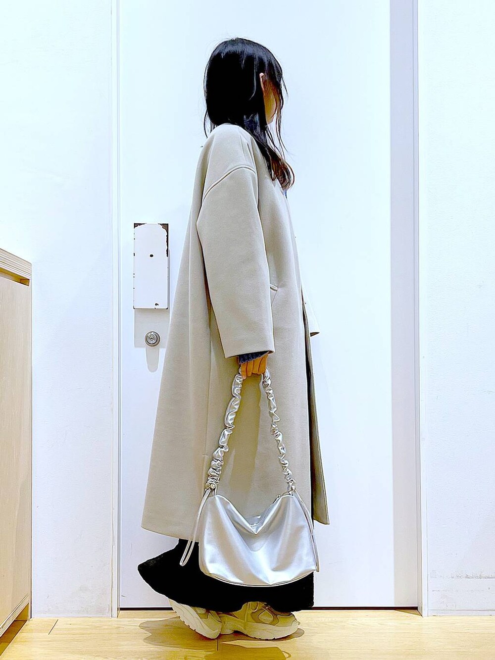シルバー系のショルダーバッグ、ベージュ系のスニーカー、ベージュ系のノーカラーコートを着用したレディースの冬コーディネートの4枚目の写真