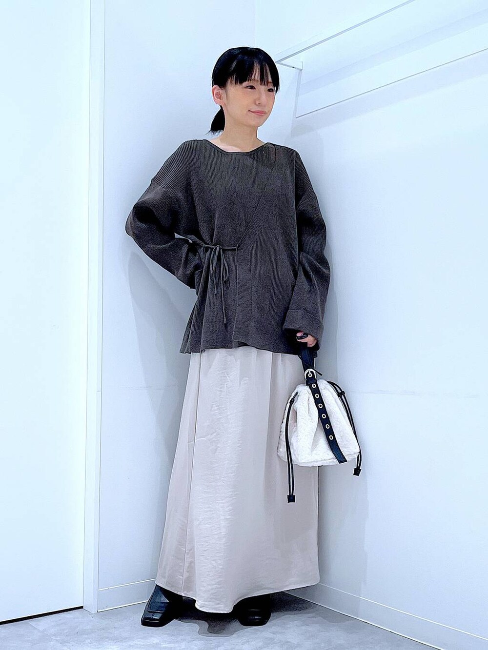 ホワイト系のハンドバッグ、ベージュ系のスカート、ブラック系のブーツを着用したレディースの秋コーディネートの2枚目の写真