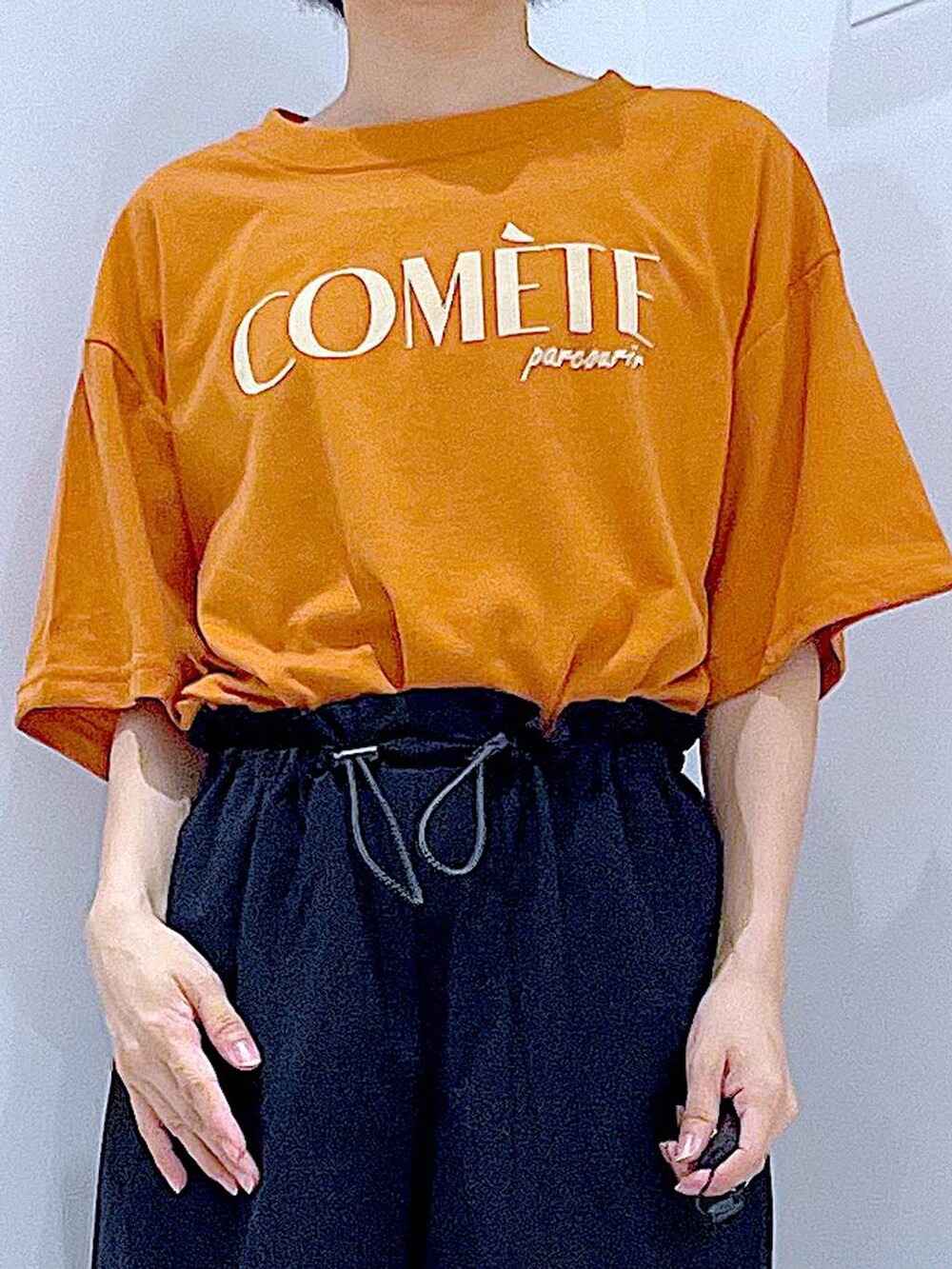 ベージュ系のショルダーバッグ、ブラック系のサンダル、オレンジ系のTシャツ/カットソーを着用したレディースの夏コーディネートの7枚目の写真