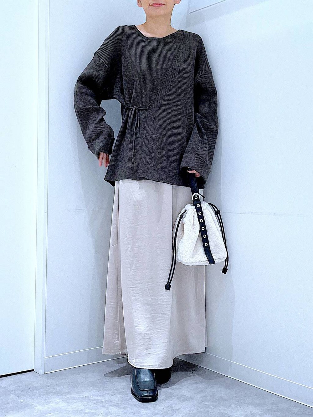 ホワイト系のハンドバッグ、ベージュ系のスカート、ブラック系のブーツを着用したレディースの秋コーディネートの6枚目の写真