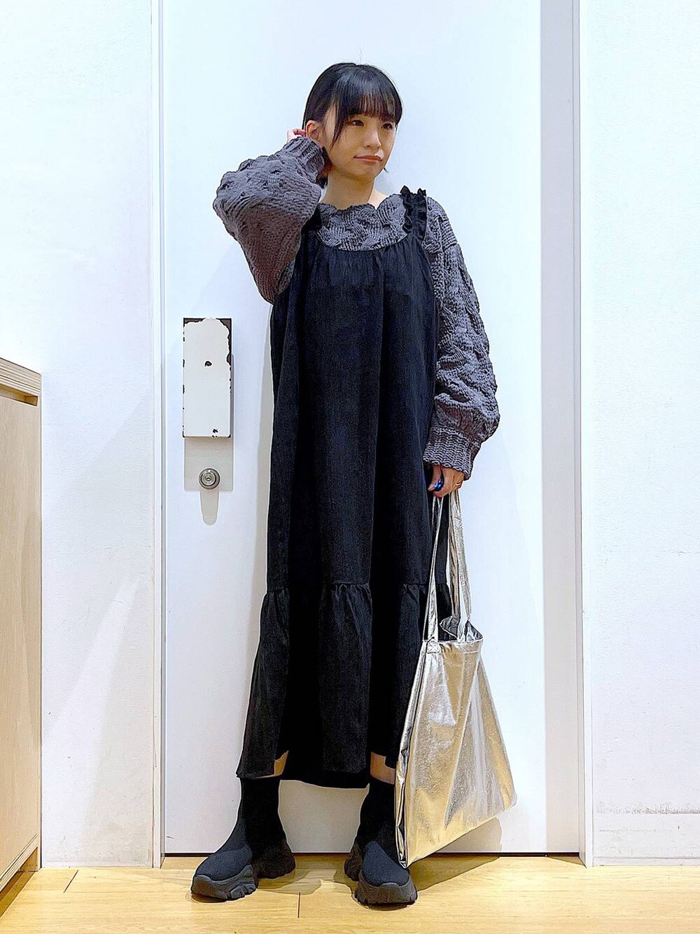 シルバー系のトートバッグ、ブラック系のブーツ、グレー系のニット/セーターを着用したレディースの冬コーディネートの2枚目の写真