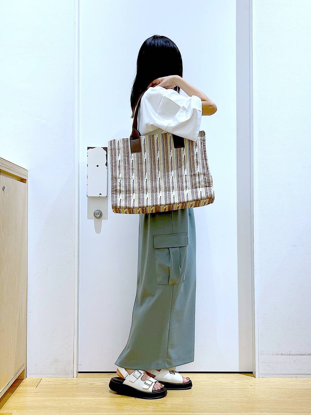 ホワイト系のサンダル、グリーン系のスカート、ブラウン系のトートバッグを着用したレディースの夏コーディネートの4枚目の写真