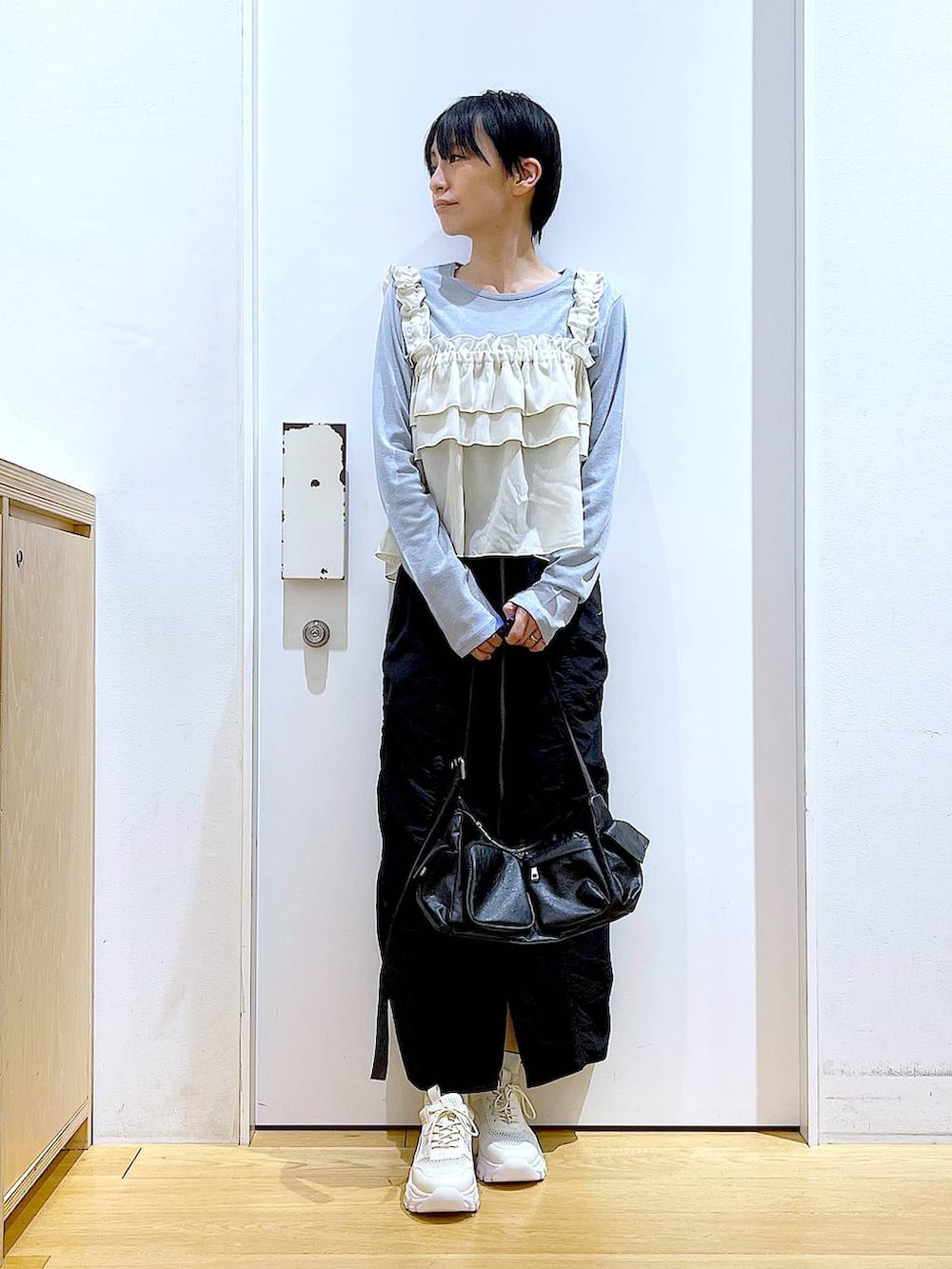 ブラック系のスカート、ブラック系のショルダーバッグ、ホワイト系のスニーカーを着用したレディースの春コーディネートの2枚目の写真