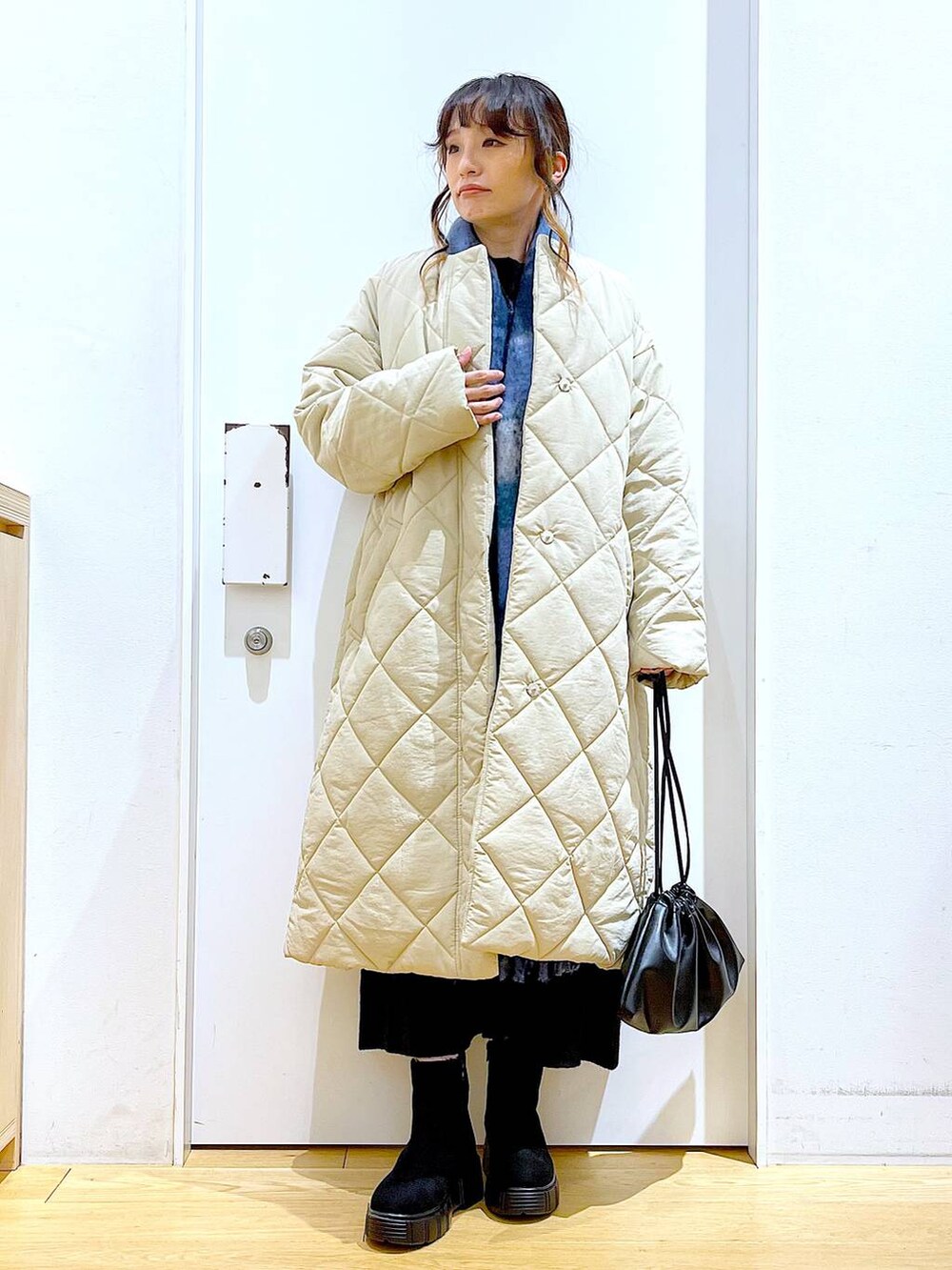 ブラック系のショルダーバッグ、ブラック系のブーツ、ベージュ系のノーカラーコートを着用したレディースの冬コーディネートの2枚目の写真