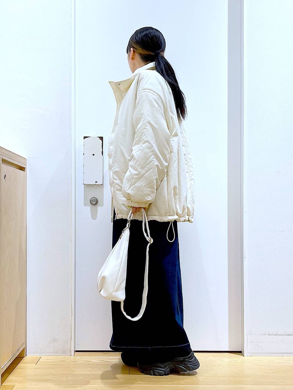 グリーン系のニット/セーター、ブルー系のジャンパースカート、ホワイト系のボディバッグ/ウエストポーチを着用したレディースの冬コーディネートの3枚目の写真