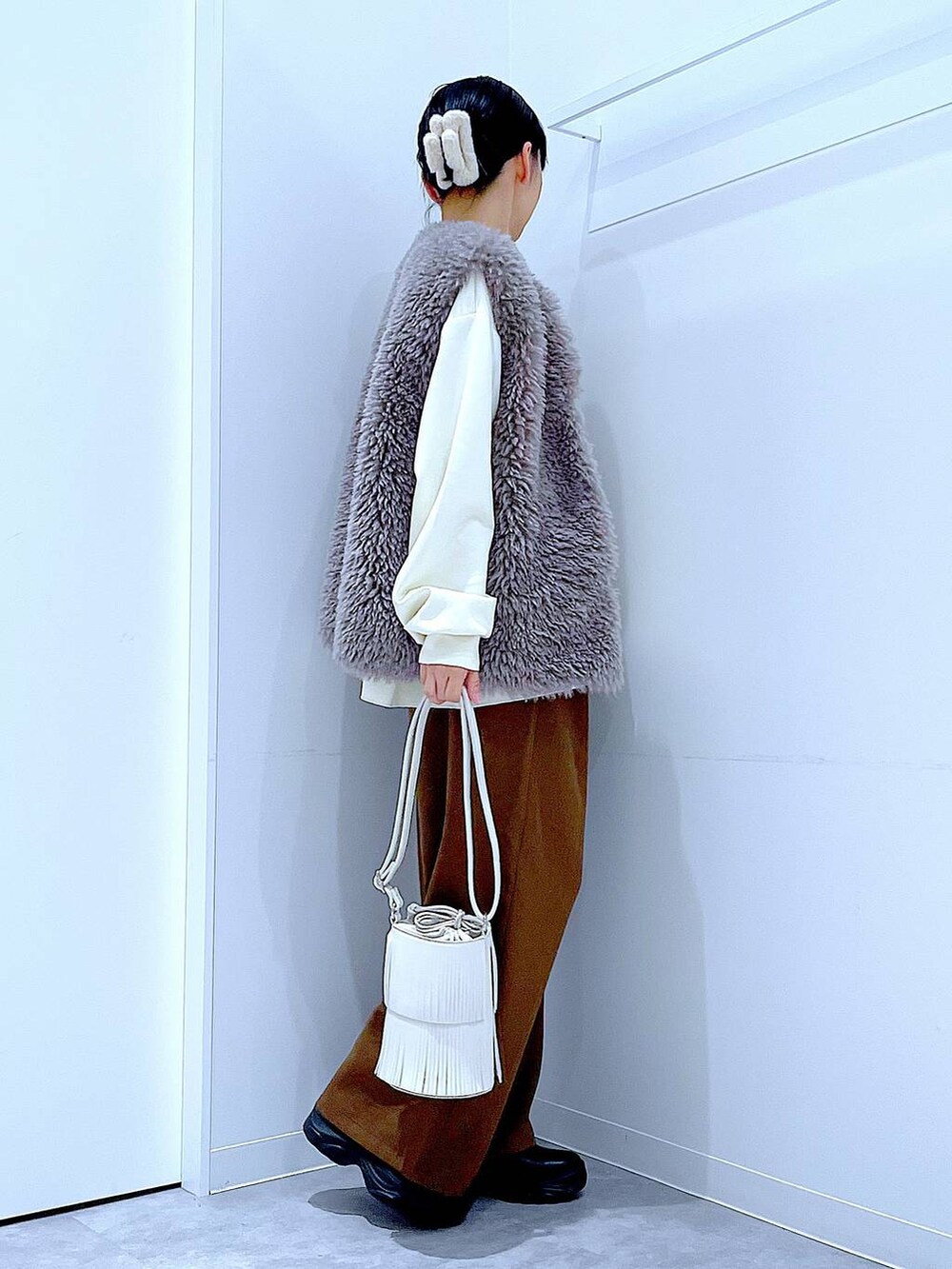 グレー系のベスト、ホワイト系のショルダーバッグ、ブラック系のブーツを着用したレディースの冬コーディネートの4枚目の写真