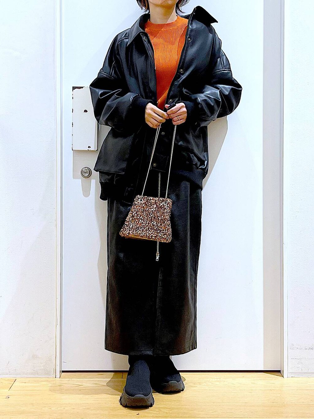 オレンジ系のニット/セーター、ブラウン系のスカート、ブラック系のブーツを着用したレディースの冬コーディネートの6枚目の写真