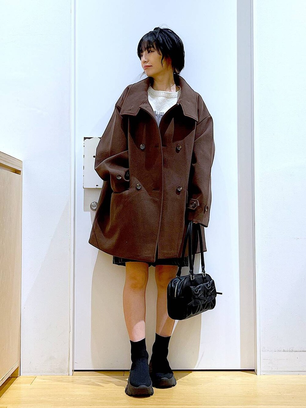 ブラウン系のステンカラーコート、ブラック系のハンドバッグ、ブラック系のブーツを着用したレディースの冬コーディネートの2枚目の写真