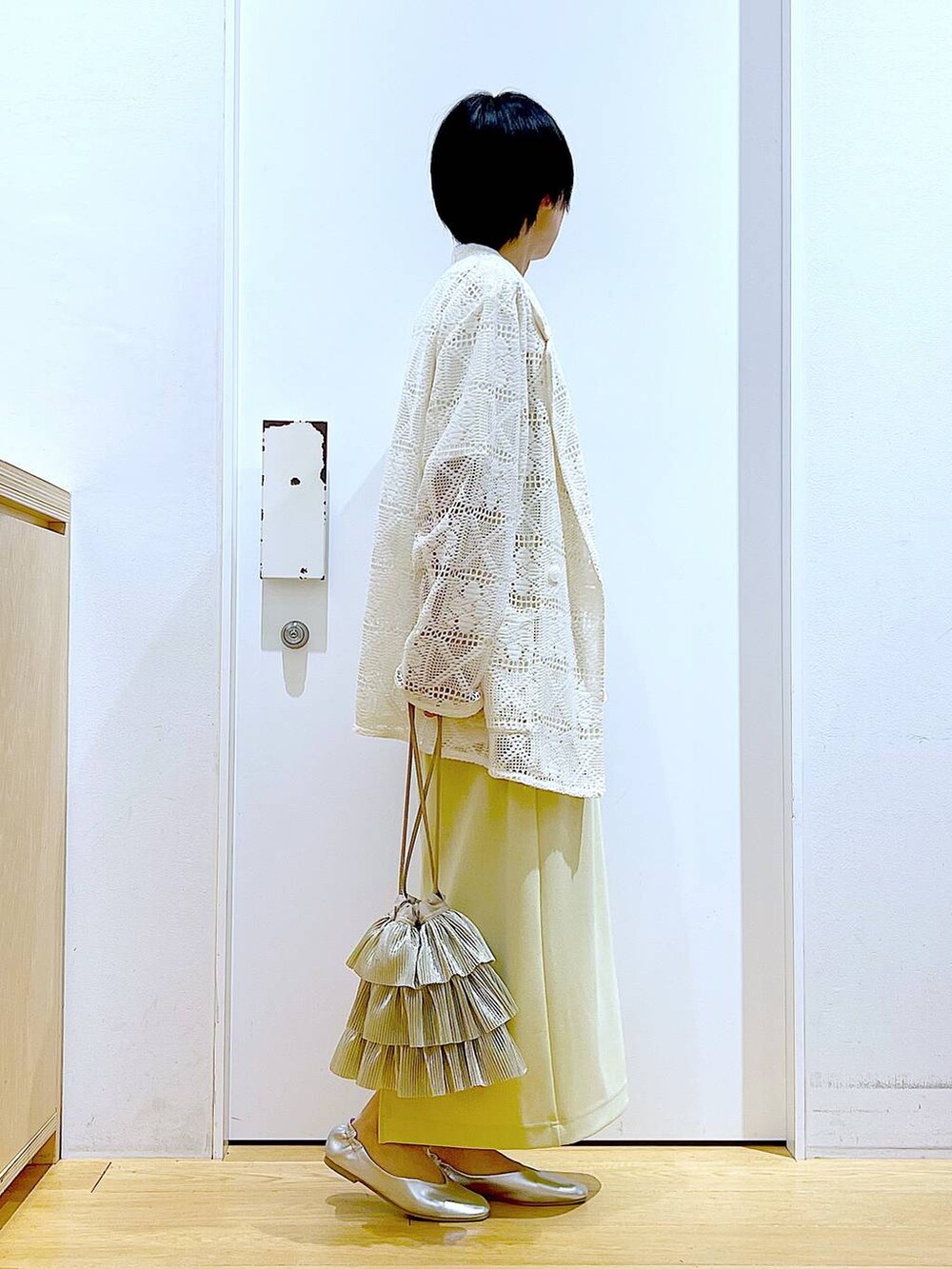 シルバー系のパンプス、ベージュ系のショルダーバッグ、イエロー系のスカートを着用したレディースの春コーディネートの4枚目の写真