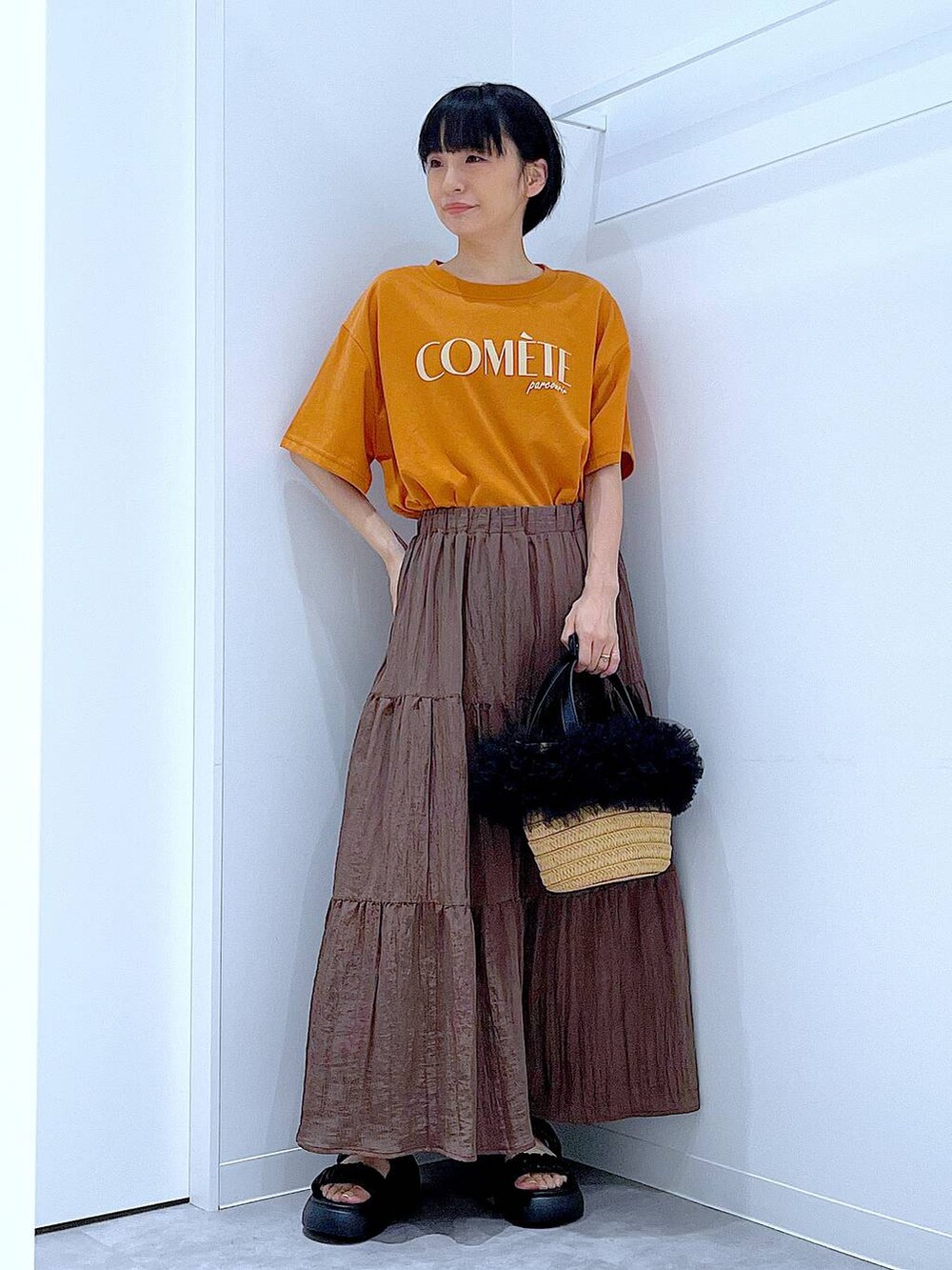 ベージュ系のショルダーバッグ、ブラック系のサンダル、オレンジ系のTシャツ/カットソーを着用したレディースの夏コーディネートの2枚目の写真