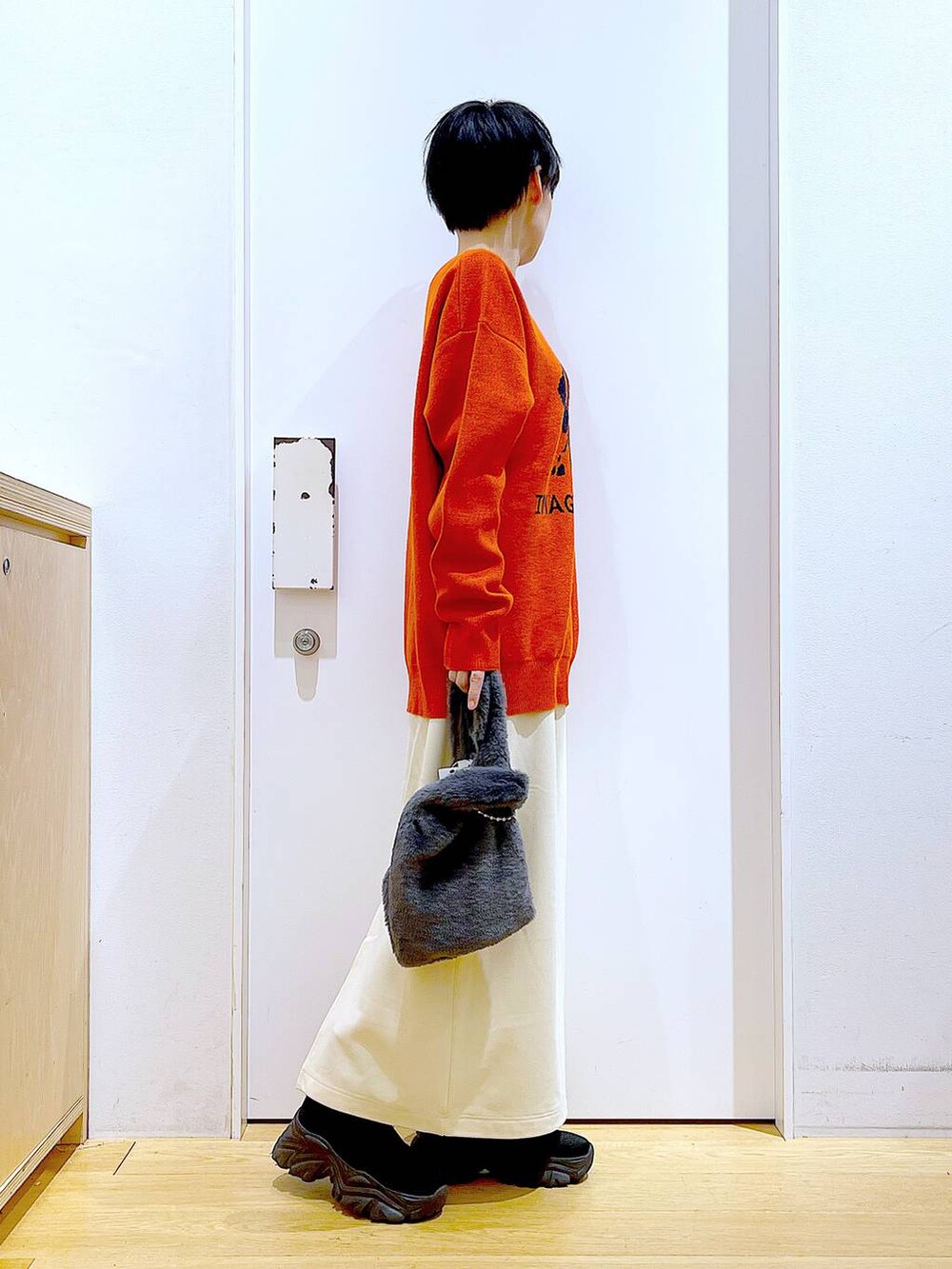 グレー系のショルダーバッグ、オレンジ系のニット/セーター、ブラック系のブーツを着用したレディースの冬コーディネートの4枚目の写真