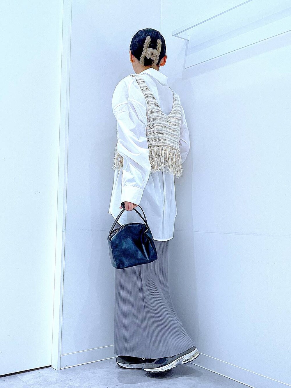 ブラック系のショルダーバッグ、ベージュ系のベスト、グレー系のスカートを着用したレディースの春コーディネートの3枚目の写真