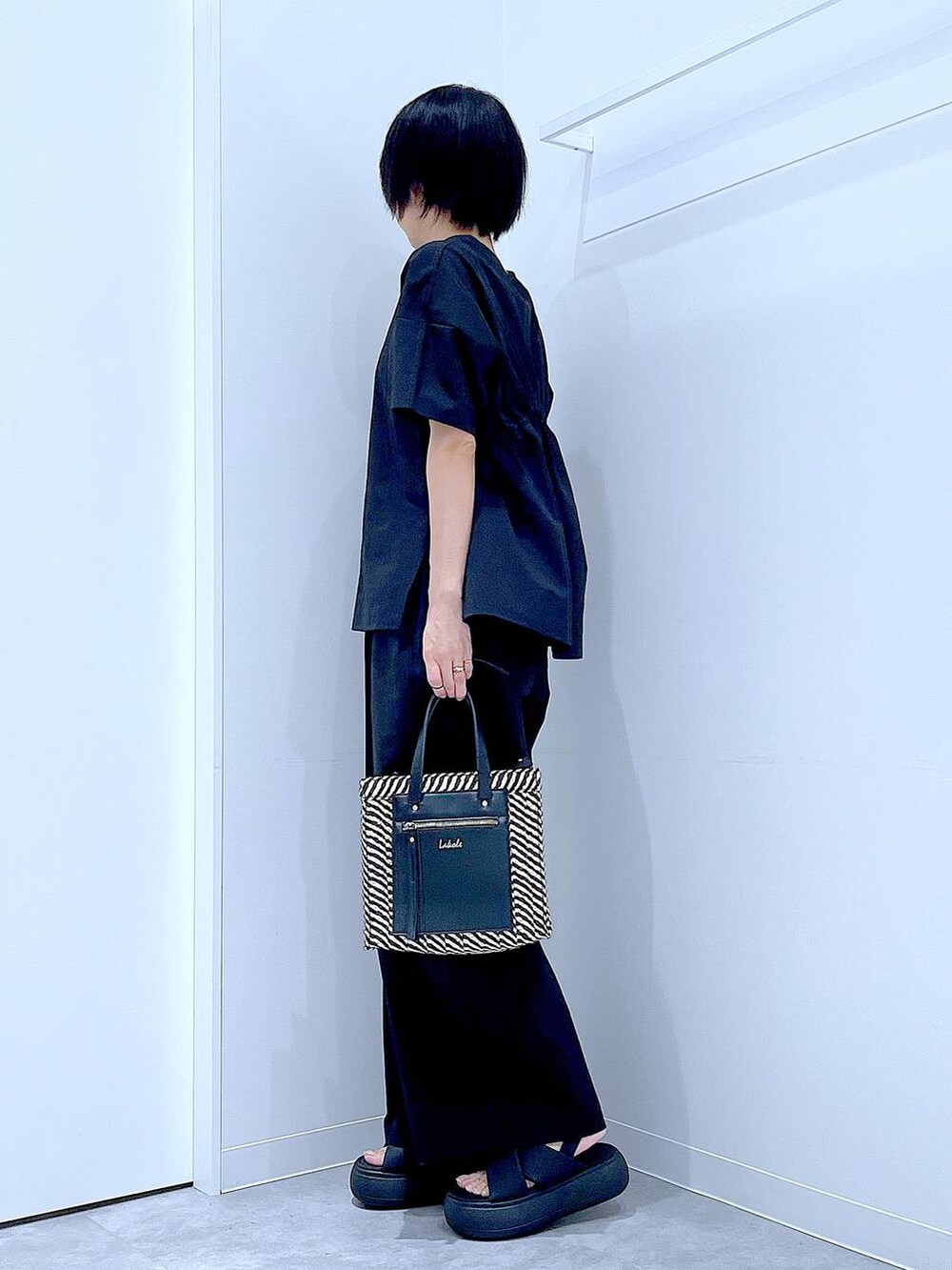 ブラック系のショルダーバッグ、ブラック系のサンダル、ブラック系のTシャツ/カットソーを着用したレディースの夏コーディネートの3枚目の写真