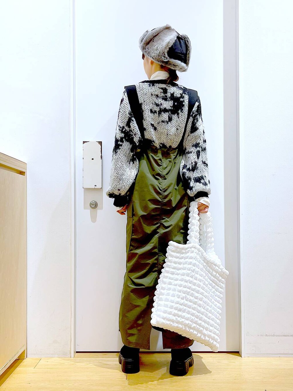 ホワイト系のトートバッグ、ベージュ系のTシャツ/カットソー、グリーン系のジャンパースカートを着用したレディースの冬コーディネートの5枚目の写真