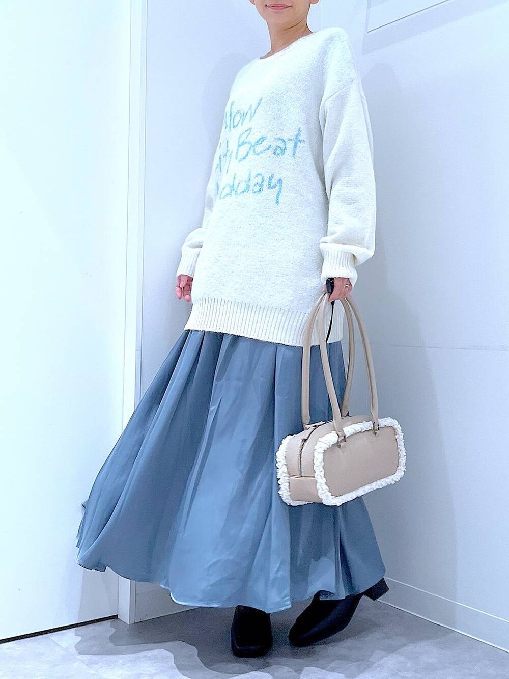 ブラック系のブーツ、ブルー系のスカート、ベージュ系のボストンバッグを着用したレディースの冬コーディネートの6枚目の写真